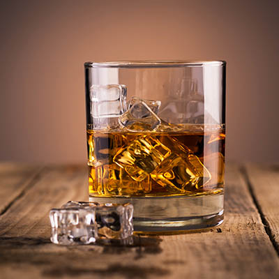 Whiskey in a glass over ice cubes, on wooden table